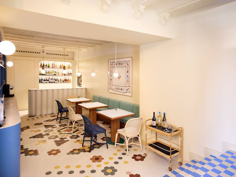 Un restaurante con piso de patrón hexagonal, mesas y sillas de madera, una zona de bar con estanterías llenas de botellas y una sección de piso a cuadros.