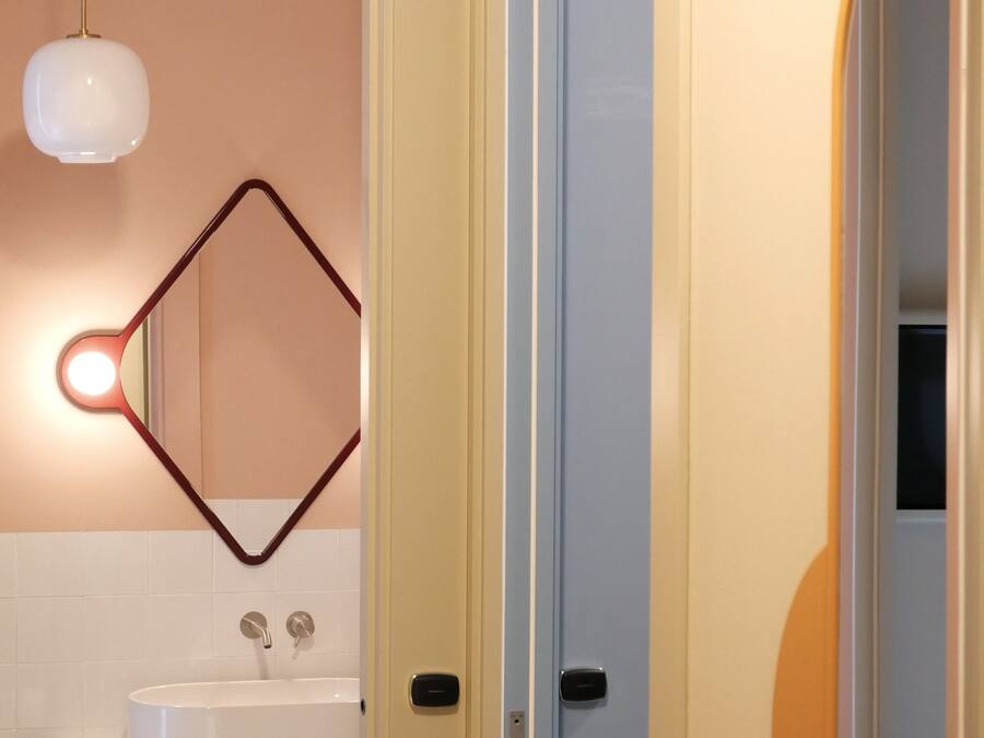 Un baño con un lavamanos blanco, un espejo de marco geométrico y una lámpara colgante.