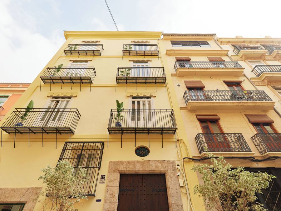 A multi-story building with balconies, a central entrance, and a small window with a decorative grille.