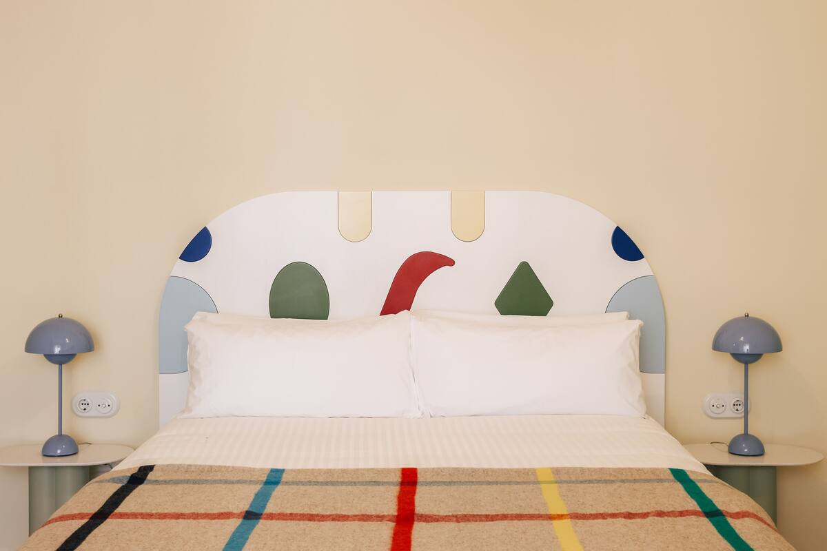 Un llit amb llençols rayats, un capçal amb motius de tall i petites làmpades de nit.