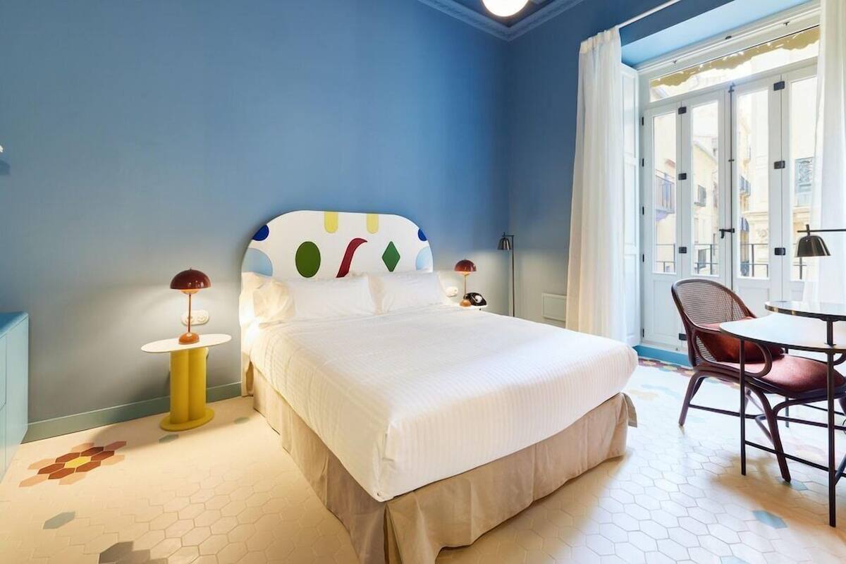 Una habitació d'hotel amb llit, una cadira, una taula i una finestra.