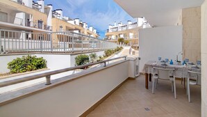 A balcony with a dining table and chairs, a railing, and a view of neighboring buildings. - Apartment "Maré Cheia SL015" with Shared Pool & Wi-Fi (Santa Luzia)