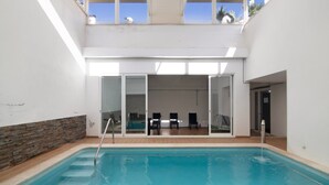 An indoor swimming pool with a clear view of the adjacent room, a stone wall, and a wooden floor. - Apartment "Maré Cheia SL015" with Shared Pool & Wi-Fi (Santa Luzia)