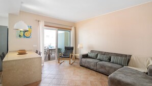 A living area with a sofa, a chair, a small table, and a lamp. - Apartment "Maré Cheia SL015" with Shared Pool & Wi-Fi (Santa Luzia)