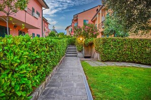A pathway leading to a building with a staircase, surrounded by well-maintained hedges and grass.