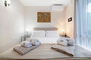 Ein Hotelzimmer mit einem Bett, zwei Nachttischen, einer Wandklimaanlage, einem Bild und einem Fenster mit Vorhängen.