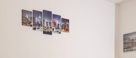 A neatly made bed with a striped blanket, a headboard, two bedside lamps, and a cityscape artwork on the wall.