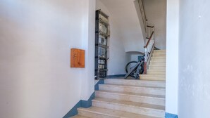 Eine Treppe mit hölzernem Geländer, ein Fahrrad, das an der Wand lehnt, und ein Regalsystem mit verschiedenen Gegenständen.