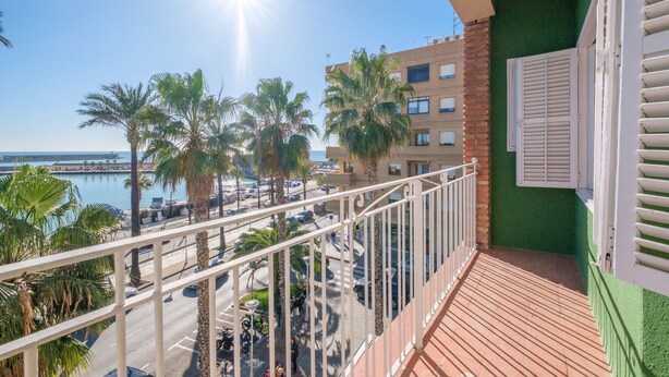 Ein Balkon mit Blick auf einen Yachthafen, Palmen und ein Gebäude mit grüner Fassade.