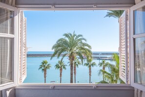 Ein Fenster mit Blick auf ein ruhiges Meer, Palmen und einen entfernten Steg.