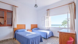 Une chambre avec deux lits, un bureau en bois, une chaise, une fenêtre donnant sur la mer et un luminaire suspendu.
