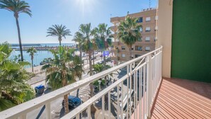 Un balcon avec vue sur une plage, des palmiers et un bâtiment situé de l’autre côté de l’eau.