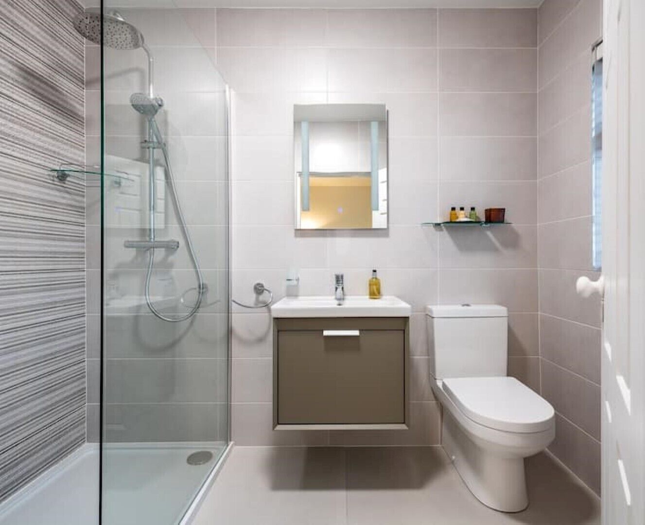 Une salle de bain moderne avec une douche à parois de verre, un lavabo blanc avec un miroir au-dessus et des toilettes.