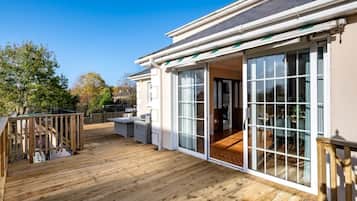 A wooden deck with outdoor furniture, a glass door leading to an interior space, and a clear blue sky.
