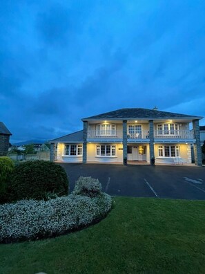 A two-story building with a balcony on the upper floor, a driveway, and well-maintained landscaping.