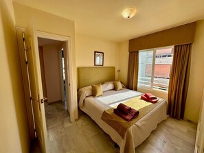 Habitació d'hotel amb un llit, una porta, una finestra amb cortines i un quadre a la paret.