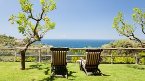 Zwei hölzerne Stühle mit Blick auf das Meer, im Vordergrund ein Holzzaun und Bäume.