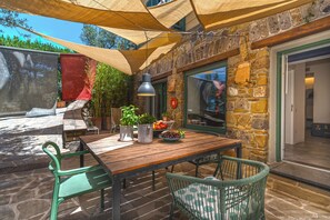 Une terrasse extérieure avec une table en bois, des chaises vertes et un mur en pierre.