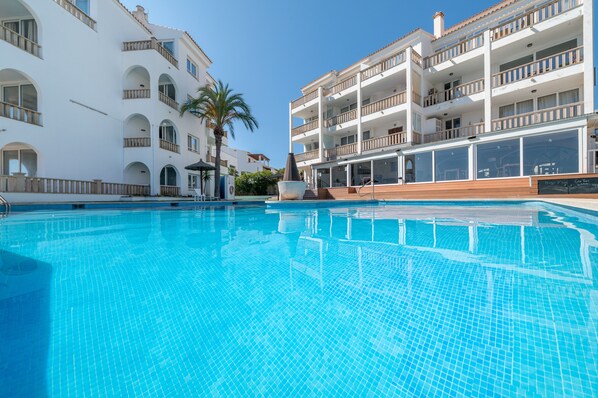 Une piscine au sol carrelé, entourée de bâtiments blancs dotés de balcons et de fenêtres en arc de cercle.