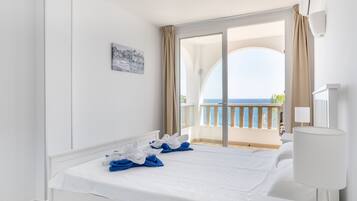 A hotel room with a bed, a nightstand, a lamp, a painting, and a view of the sea through a balcony.