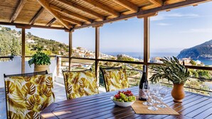 Une terrasse en bois avec une table dressée pour le dîner, offrant une vue sur une ville côtière et la mer.