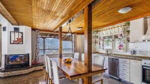 Une cuisine chaleureuse avec une table à manger en bois, des chaises, une cheminée et une vue sur les montagnes.