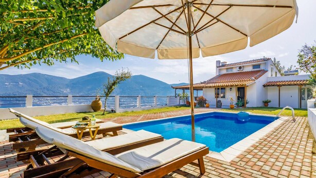 Un espace piscine avec des chaises longues et un parasol, une terrasse en briques et une vue sur la mer et les montagnes.