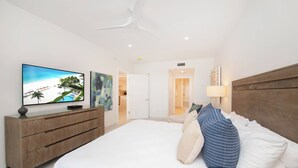 Un dormitorio con una cama grande, un televisor sobre un mueble de vidrio y una puerta que da a otra habitación.