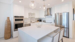 Una cocina moderna con armarios blancos, electrodomésticos de acero inoxidable e iluminación colgante.