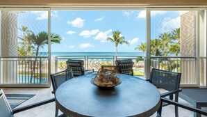 Mesa redonda com uma cesta de pão e um arranjo decorativo, com vista para uma praia com palmeiras e o oceano.