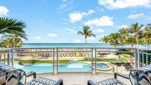 Uma varanda com piscina, espreguiçadeiras e vista para a praia e o oceano.