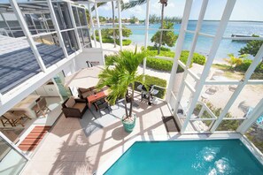 Un espace aménagé au bord de la piscine avec vue sur la mer, un coin salon avec une table et des chaises, et une grande fenêtre donnant sur l’océan.