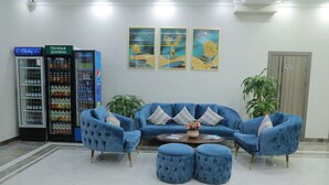 Un hall d’entrée avec un ensemble de canapés bleus, deux poufs, une machine à café et un réfrigérateur.