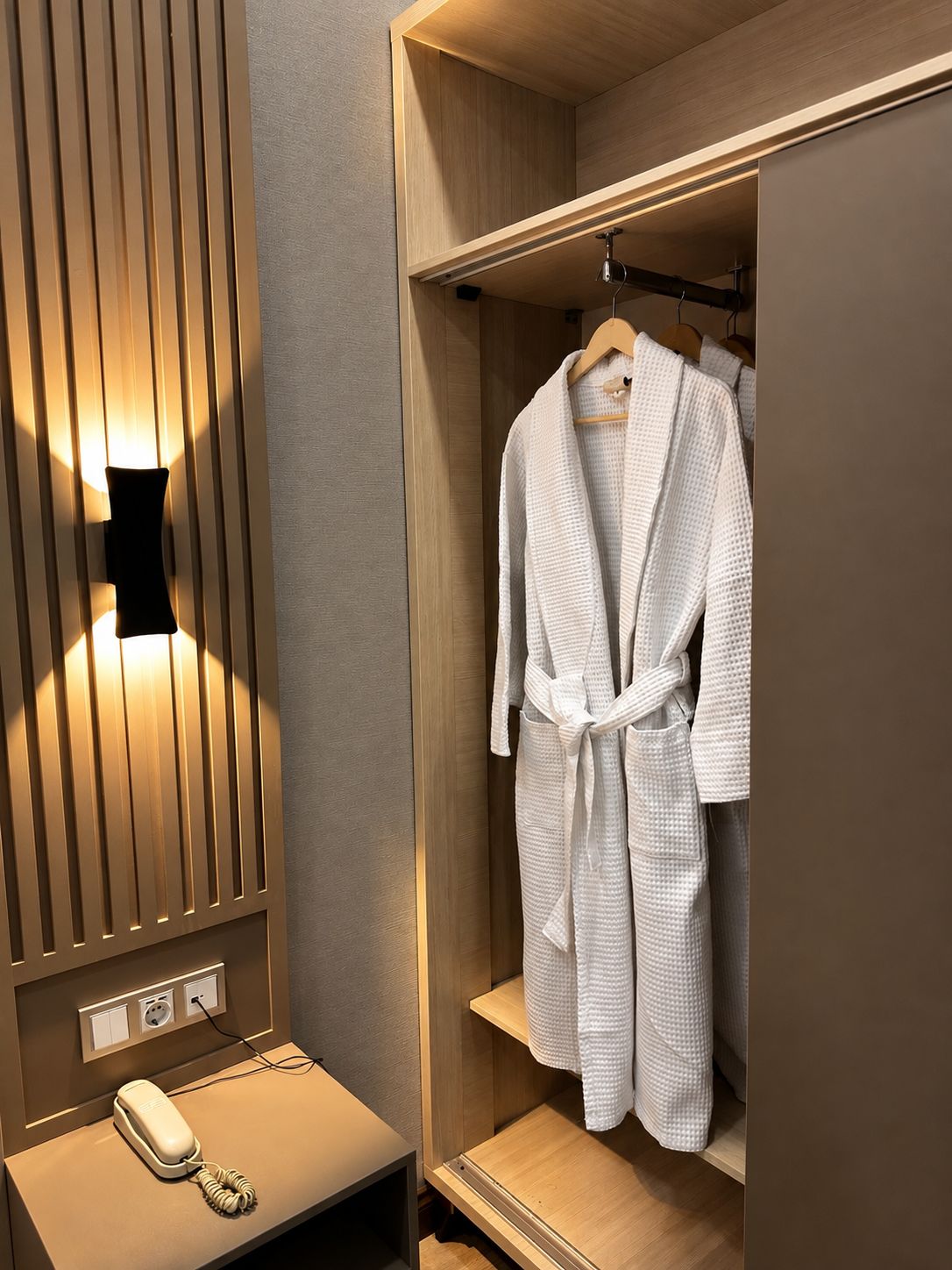 A walk-in closet with a robe hanging on a wooden hanger, a telephone on a small table, and a wall-mounted light fixture.
