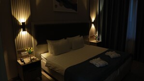 Une chambre d’hôtel avec un grand lit, des lampes de chevet, une table de chevet avec un téléphone et un vase de fleurs, et un tableau accroché au mur.