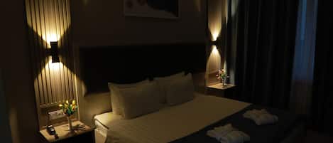 A hotel room with a large bed, bedside lamps, a nightstand with a phone and a vase of flowers, and a painting on the wall.