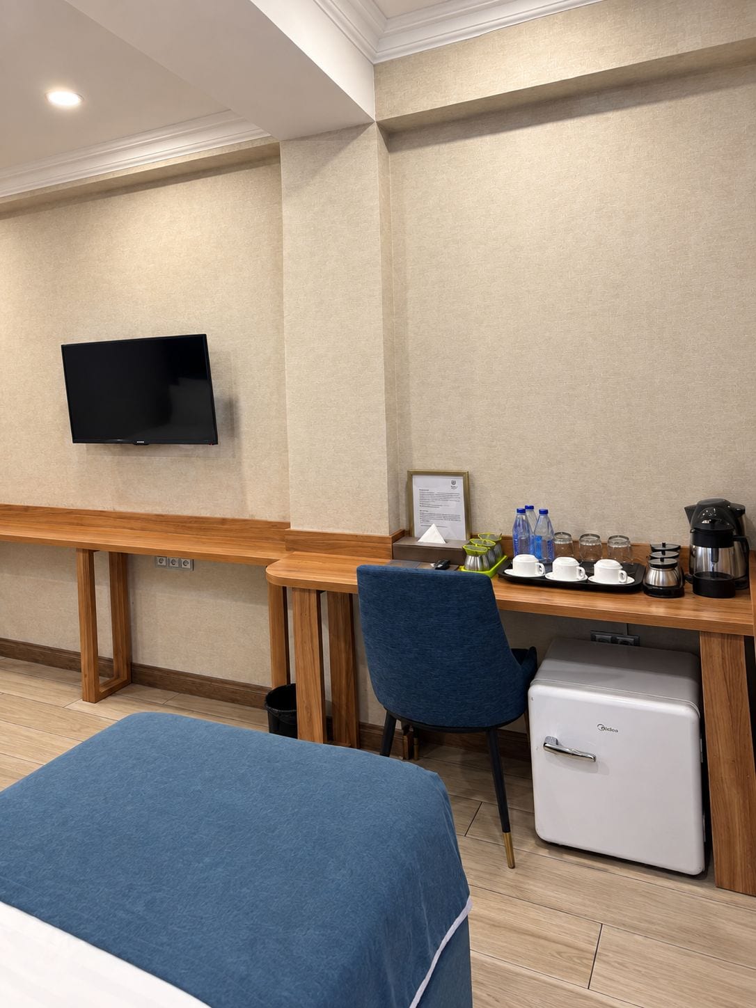 A hotel room with a bed, a desk with a computer, a coffee maker, and a mini fridge.
