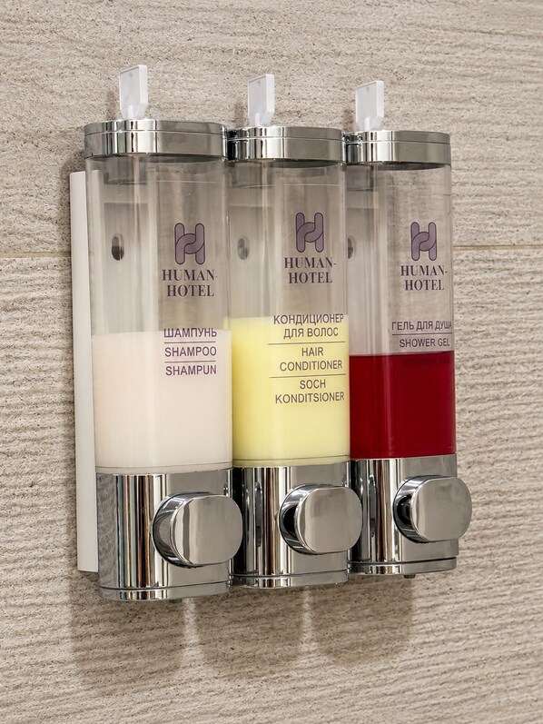 Un distributeur mural doté de trois compartiments contenant du shampoing, de l’après-shampoing et du gel douche.