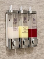 Dispensador de pared con tres compartimentos que contienen champú, acondicionador para cabello y gel de ducha.