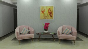 Un espace d’accueil avec deux fauteuils roses, une petite table sur laquelle est posé un vase de fleurs, et un tableau accroché au mur.