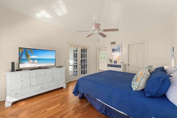 A bedroom with a bed, a TV on a dresser, a ceiling fan, and a door leading to a balcony.