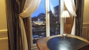 A hotel room with a view of a cityscape through a large window, featuring a lamp on a wooden table. - Lafayette 75 M2 (Paris)
