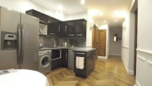 A modern kitchen with a built-in washer and dryer, a refrigerator, and a small island with a sink. - Lafayette 75 M2 (Paris)