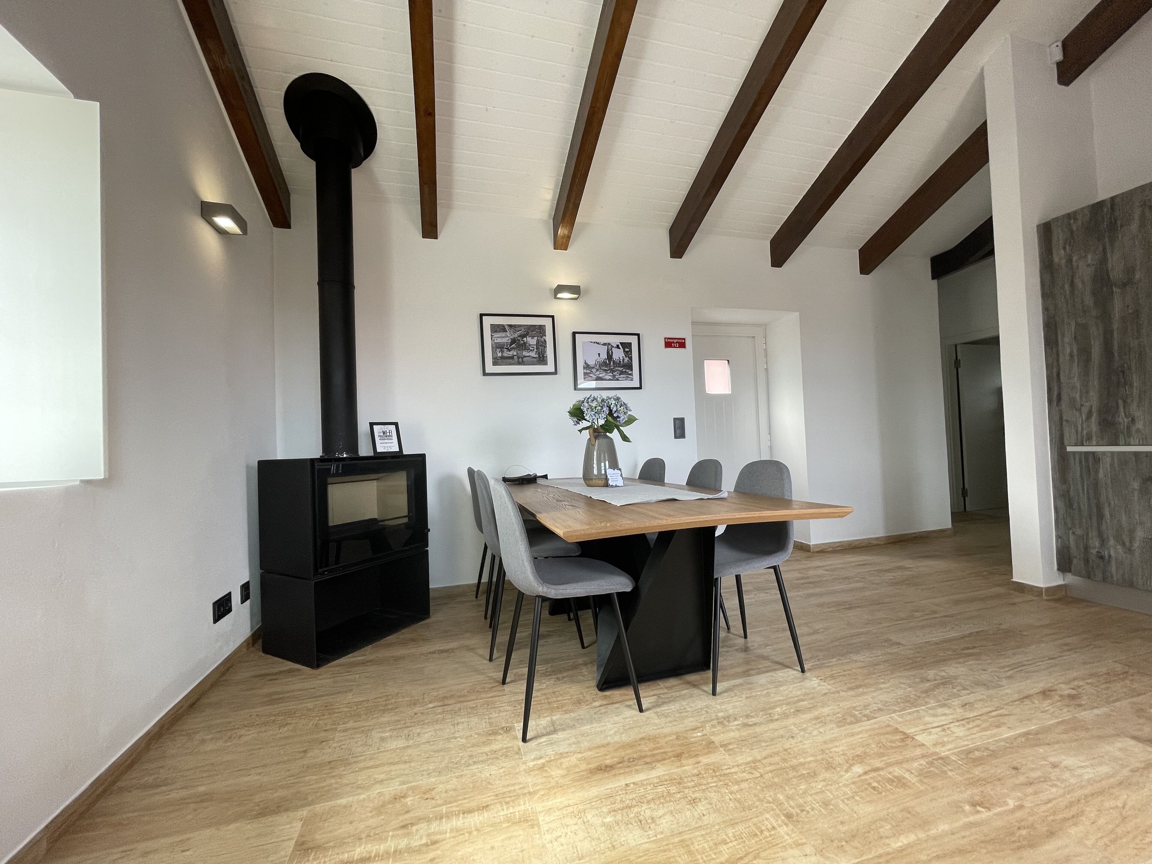 A dining area with a wooden table, grey chairs, a black stove, and framed pictures on the wall.