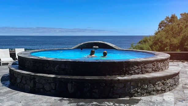 A circular infinity pool with two levels, surrounded by stone steps, overlooking a clear blue sea. - Stylish 2 Bedroom Stone House With Stunning Views, São Jorge, Azores (Vista) (São Jorge)