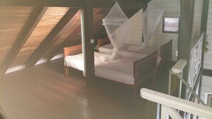 Un dormitorio con cama bajo un techo inclinado, mosquitero y ventilador.