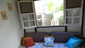 Un rincón acogedor con un banco acolchado, una mesita con un florero y una ventana con contraventanas.