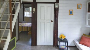 Una habitación con una escalera, una cama, una mesita con un florero y una puerta blanca.