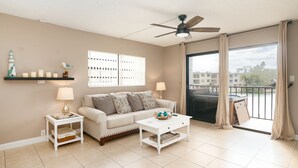 A living room with a sofa, two side tables, a coffee table, a ceiling fan, and a large window with curtains.