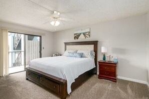 Een slaapkamer met een groot bed, een nachtkastje, een dressoir, een plafondventilator en een schuifdeur naar een balkon.